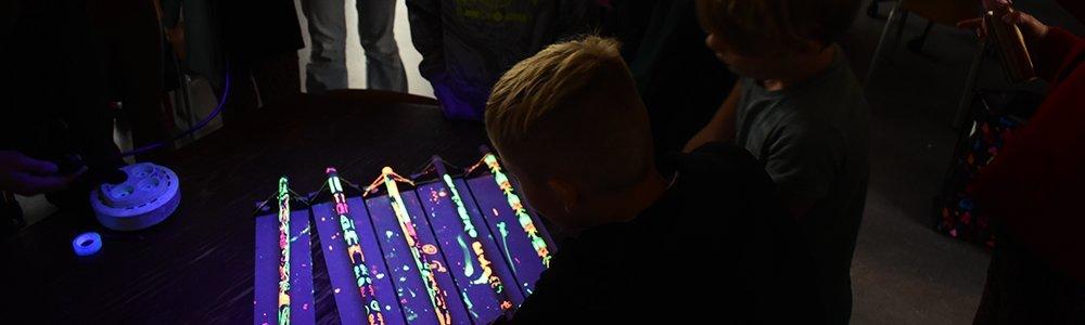 We zien een kind bij een beschilderde bamboekstok die oplicht in het UV licht.